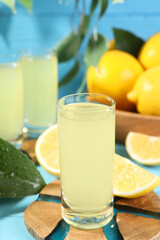 Tasty limoncello liqueur and lemons on light blue table, closeup