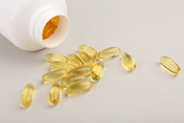 Vitamin capsules and bottle on light grey background, closeup