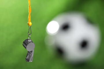Football referee equipment. Metal whistle on blurred green background, closeup with space for text