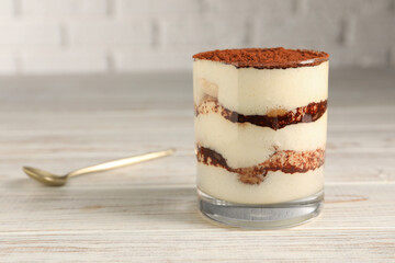 Delicious tiramisu in glass on light wooden table, closeup. Space for text