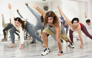 Focused adult man doing stretching workout with group of people before dance training in choreography class
