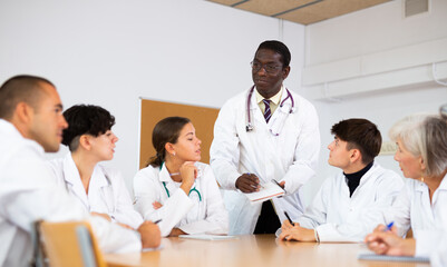 Fototapeta premium African American professor of medicine giving lecture to group of interested internship doctors sitting at same table in professional seminar