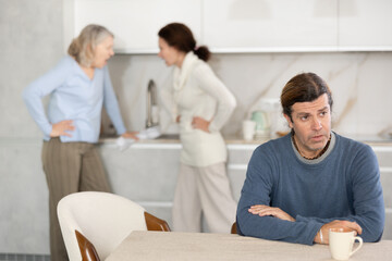 Obraz premium Old woman is quarreling with woman while sad man is sitting with them in kitchen