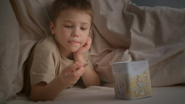 The boy throws a coin into the piggy bank before going to bed, dreaming about something. Accumulation of funds for their own needs. Money as capital since childhood.