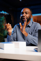 African american entertainer presenting mobile phone from brand sponsoring video, urging viewers to...