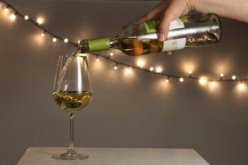 Close-up of a bartender's hand pouring white wine from a bottle into a glass in an intimate lighting of a bar or festive setting