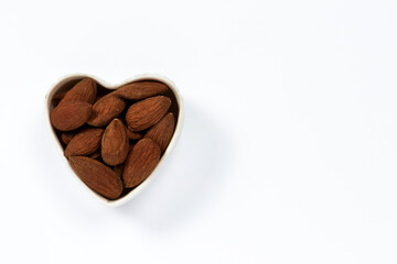Raw almonds in a heart-shaped white ceramic bowl isolated on white