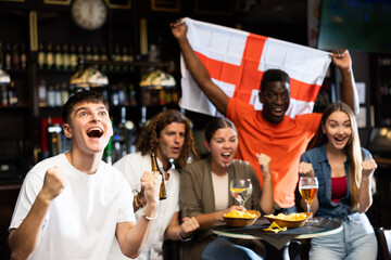 Glad males and females with England flag clinking glasses with beer on party in bar