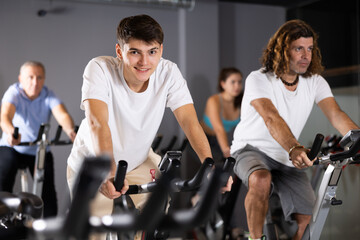 Men and woman taking indoor cycling class at fitness center, doing cardio riding bike