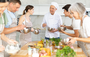 Elderly man cook in uniform teaches group of different people how to cook dish