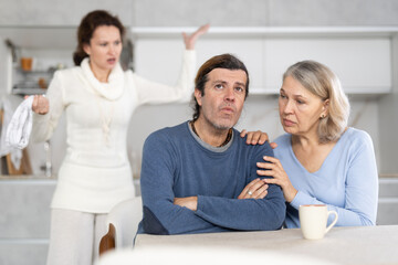 Woman scolding man at kitchen while old woman calming him down