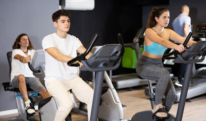 Fototapeta na wymiar Group of people of different ages working out on stationary bicycle in gym. Physical activity and fitness concept