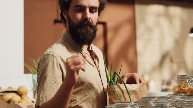 Vegan man in zero waste supermarket using biodegradable paper bag while shopping for healthy pantry staples. Client in local grocery shop with no single use plastics policy