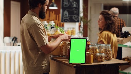 Client shops next to chroma key tablet with copy space used as commercial sign in zero waste supermarket. Promotional ad on green screen device in food store with products in nonpolluting package