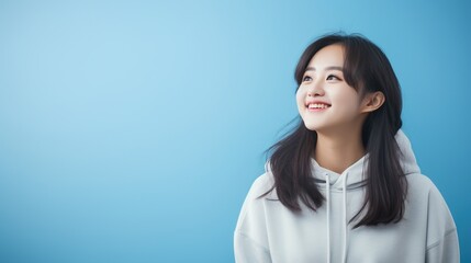 Obraz premium Smiling young Asian woman in a white hoodie looking to the side