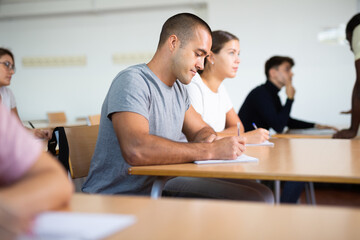 Portrait of interested focused man sitting at desk at lesson in school auditorium. Adult learning and education concept