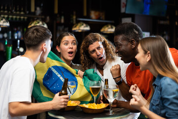 Group of Brazil football team fans spending time in bar, drinking bear and having fun. People with...