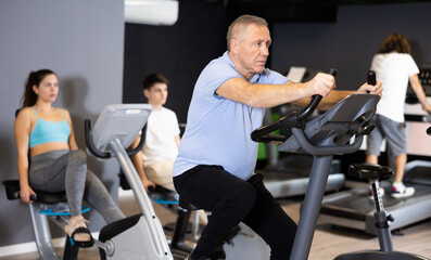 Mature man doing cardio workout out at gym, training on exercise bikes