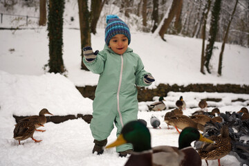 Cheerful baby boy playing with birds at the park in winter