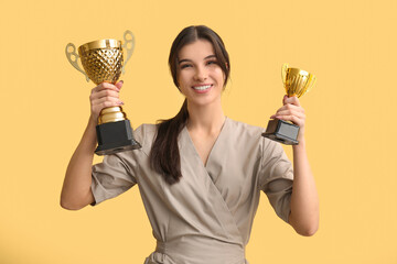 Young cosmetologist with gold cups on yellow background