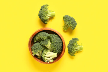 Wooden bowl with fresh broccoli cabbages on yellow background