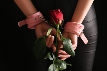 Woman with beautiful red rose flower and handcuffs from sex shop on black background, back view