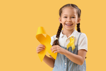 Cute little girl with yellow ribbons on color background. Childhood cancer awareness concept