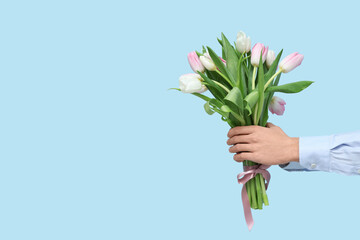Male hands with bouquet of beautiful tulips on blue background. International Women's Day