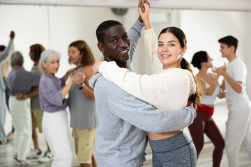 Portrait of young girl and adult African American man practicing in modern choreography studio, dancing slow ballroom dances in pair..