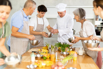 Adult male cook in uniform teaches group of different people how to cook dish