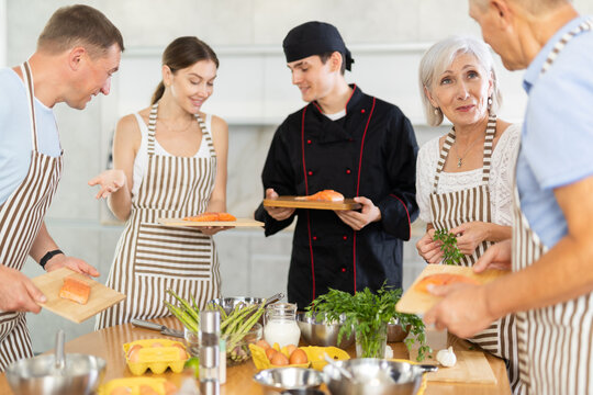 Friendly smiling elderly woman talking to culinary enthusiasts during group cooking masterclass..