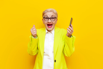 old grandmother in business clothes blazer and glasses uses a smartphone and celebrates victory...