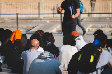 Group of tourists sitting during outdoor excursion tour in the city streets with guide, a docent...