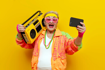 old funny grandmother in youth costume dances with tape recorder and listens to music on yellow...