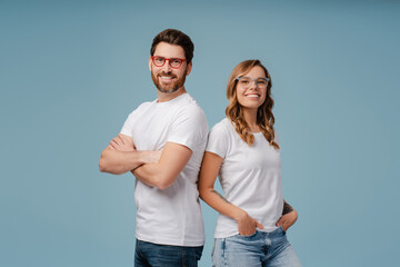 Portrait of successful smiling man and woman wearing white t shirt and stylish glasses isolated on blue background. Happy attractive fashion models with arms crossed posing for pictures in studio