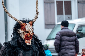 Krampus demon on blurred street background.Carnival processions in Germany. Carnival costumes and characters.Winter costume processions on the streets of Europe.Demon face of Krampus monster. - obrazy, fototapety, plakaty