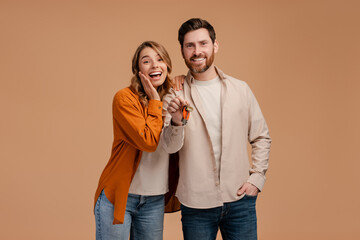 Smiling young couple holding keys from new house isolated on beige background. Happy man and woman...