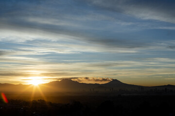 Sun shining behind volcanoes in Mexico City
