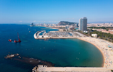 Aerial panoramic view of modern Barcelona cityscape on Mediterranean coast overlooking famous marina Olympic Harbour on sunny summer day, Spain