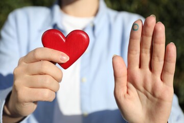 Woman showing blue circle as World Diabetes Day symbol and red heart outdoors, closeup