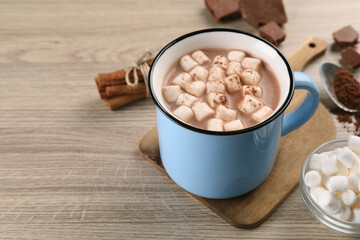 Cup of aromatic hot chocolate with marshmallows, and cocoa powder on wooden table, closeup. Space for text