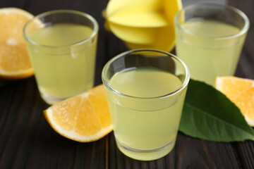 Tasty limoncello liqueur, lemon and green leaf on dark wooden table, closeup