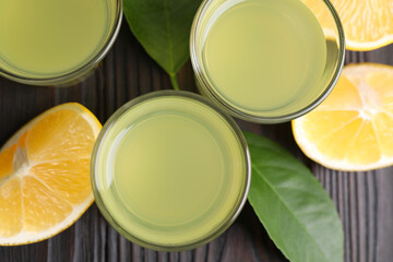 Tasty limoncello liqueur, lemon and green leaves on dark wooden table, flat lay