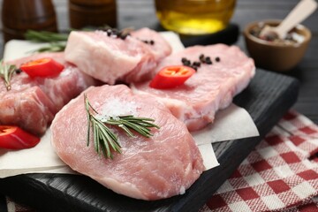 Pieces of raw pork meat with chili pepper and spices on table, closeup