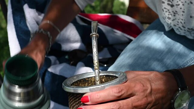 horizontal video in slow motion of woman's hands with painted nails drinking Argentine mate in the shade of a tree in summer 3