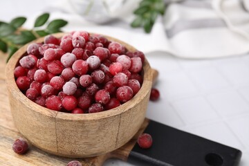 Frozen red cranberries in bowl on white tiled table, closeup. Space for text
