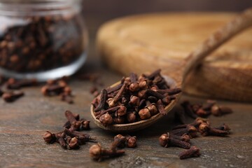Spoon with aromatic cloves on wooden table, closeup