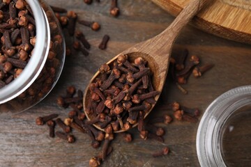 Glass jar and spoon with aromatic cloves on wooden table, flat lay