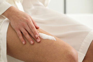 Obraz na płótnie Canvas Woman applying self-tanning product onto leg indoors, closeup