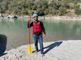 a man is standing by the water holding a raft and paddle © Wirestock